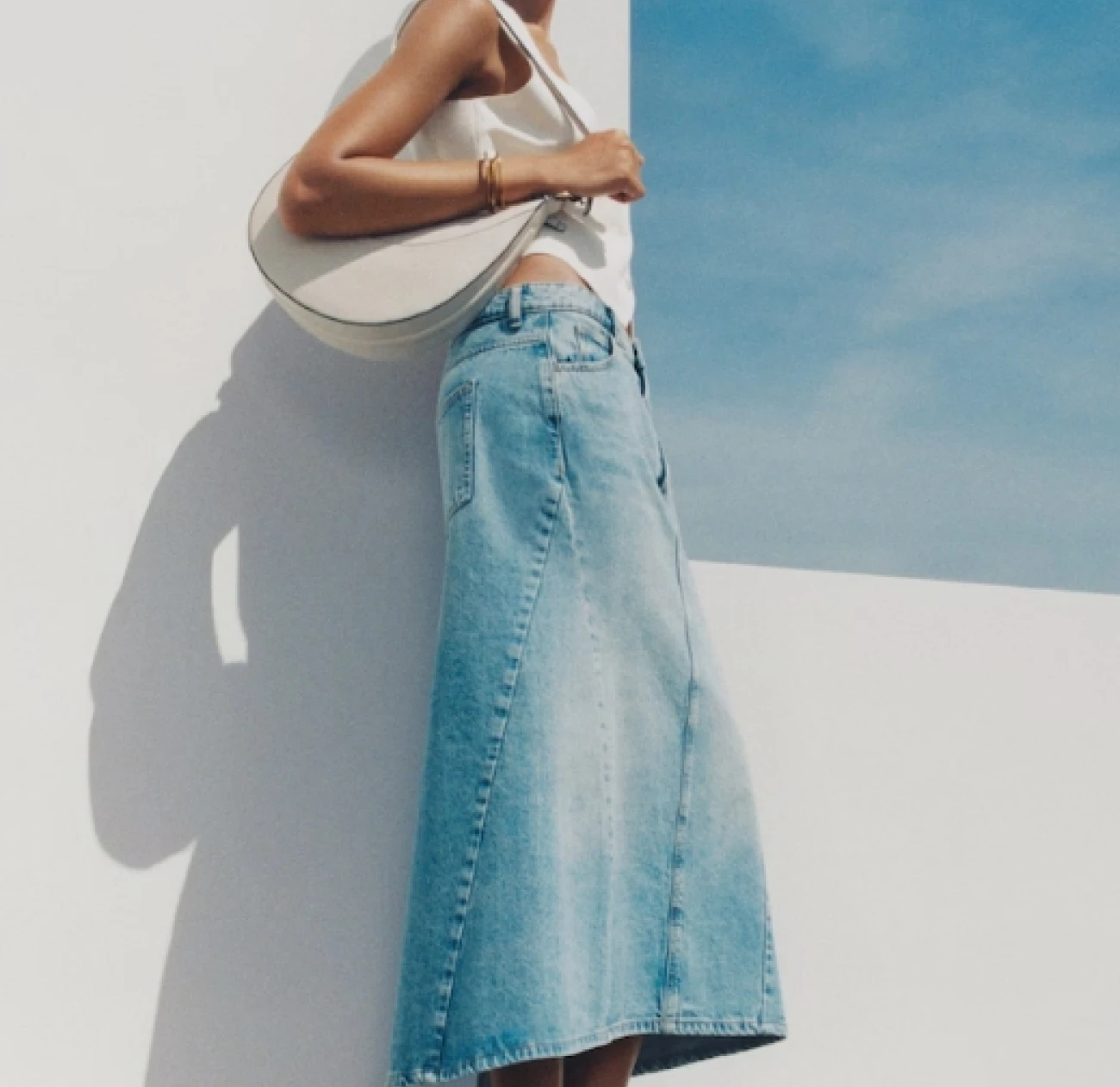 A model wearing an asymmetric long denim skirt available on the mango fashion label website currently on sale at 50% off. this long denim skirt is one of our top summer/autumn picks for the elevated wardrobe