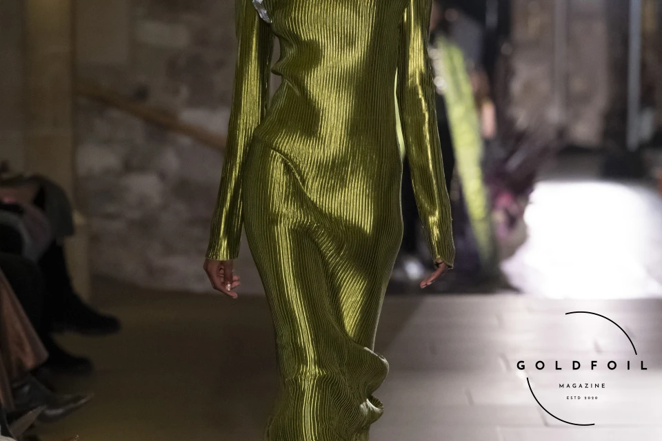 Mithridate AW24 at London Fashion Week included this stunning floor length close to body cut dress in metallic gold accessorised with a beautiful hand made flower on the right shoulder. Mithridate AW24 at London Fashion Week included this stunning floor length close to body cut dress in metallic gold accessorised with a beautiful hand made flower on the right shoulder.