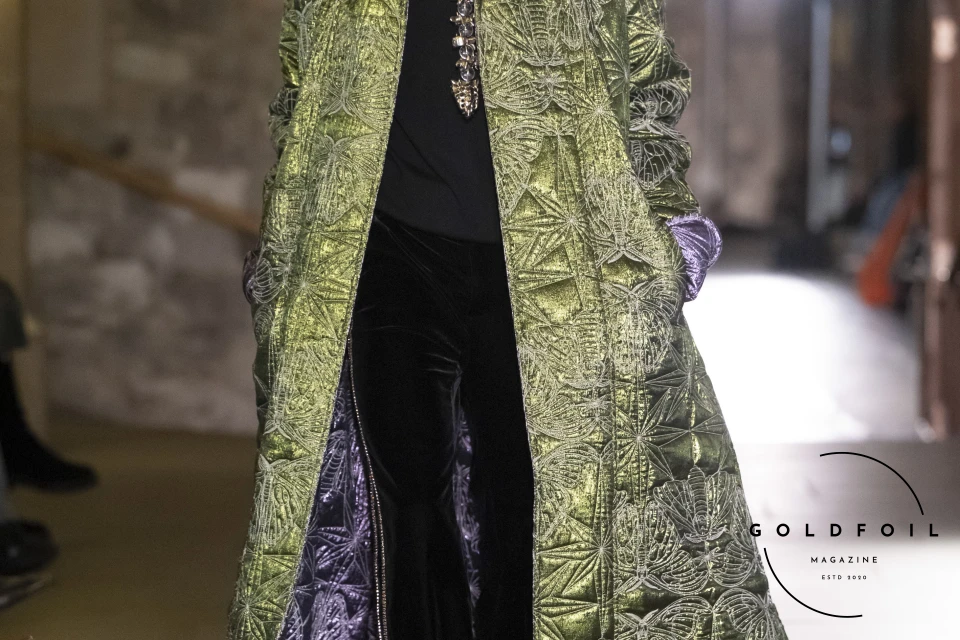 The men's look features a full black outfit of black velvet trousers and a turtle neck, with silver shoes, and a green metallic cape with intricate stitching of a moth motif. GoldFoil Magazine is a London-based fashion magazine The men's look features a full black outfit of black velvet trousers and a turtle neck, with silver shoes, and a green metallic cape with intricate stitching of a moth motif. GoldFoil Magazine is a London-based fashion magazine