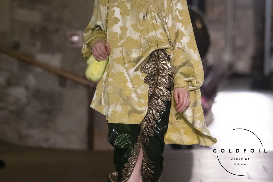 The outfit at the Mithridate AW24 collection features a bell sleeve top in gold and yellow motifs carefully blended into a velvet rich green skirt with a leaf motif at the hem The outfit at the Mithridate AW24 collection features a bell sleeve top in gold and yellow motifs carefully blended into a velvet rich green skirt with a leaf motif at the hem