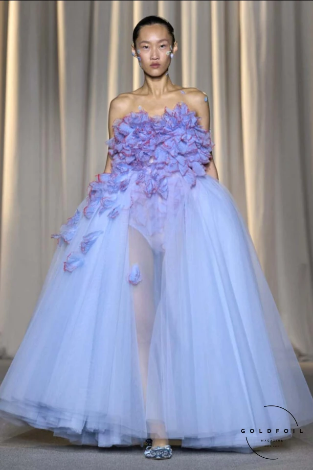 Giambattista Valli’s fall 2024 haute couture show in Paris was a vibrant spectacle, true to his signature voluminous tulle dresses while embracing an Indian influence. Held at 7 Place Vendôme, the show opened with Indian musicians and featured gowns blending Italian opulence with Indian floral motifs. Models wore bouquet-like dresses adorned with floating florals and jasmine garlands, creating a surreal mix of Valli's love for India and Botticelli-inspired paradise gardens. Giambattista Valli’s fall 2024 haute couture show in Paris was a vibrant spectacle, true to his signature voluminous tulle dresses while embracing an Indian influence. Held at 7 Place Vendôme, the show opened with Indian musicians and featured gowns blending Italian opulence with Indian floral motifs. Models wore bouquet-like dresses adorned with floating florals and jasmine garlands, creating a surreal mix of Valli's love for India and Botticelli-inspired paradise gardens.