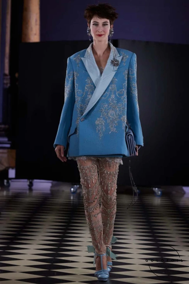 The highlight was the majestic court dress for Marie-Antoinette's statue, crafted from 1,500 meters of tulle and 120 meters of triple white silk organza, embroidered with symbols of the French court. The dress, light yet voluminous, featured intricate details like candlestick illuminations and 3D knots, embodying the timeless elegance and innovation that define both Fournié’s vision and haute couture itself. The highlight was the majestic court dress for Marie-Antoinette's statue, crafted from 1,500 meters of tulle and 120 meters of triple white silk organza, embroidered with symbols of the French court. The dress, light yet voluminous, featured intricate details like candlestick illuminations and 3D knots, embodying the timeless elegance and innovation that define both Fournié’s vision and haute couture itself.