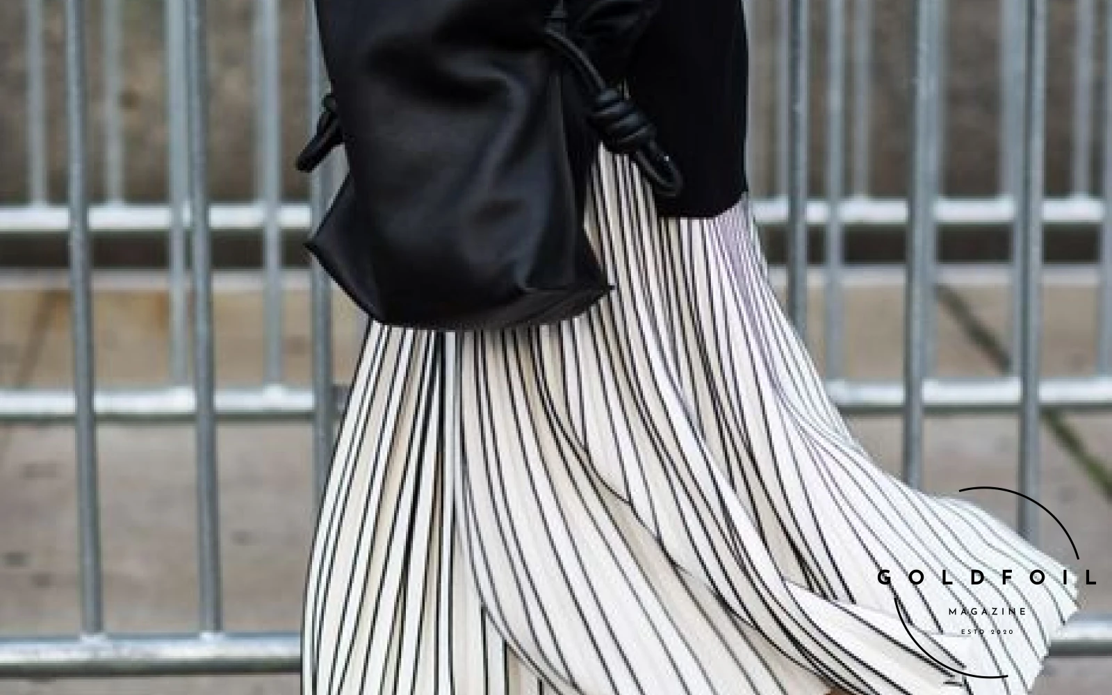 a fashionable person wearing a stripe pleated skirt in black and white, with a black velvet top, and a black leather handbag, paired with navy gazelle adidas trainers a fashionable person wearing a stripe pleated skirt in black and white, with a black velvet top, and a black leather handbag, paired with navy gazelle adidas trainers
