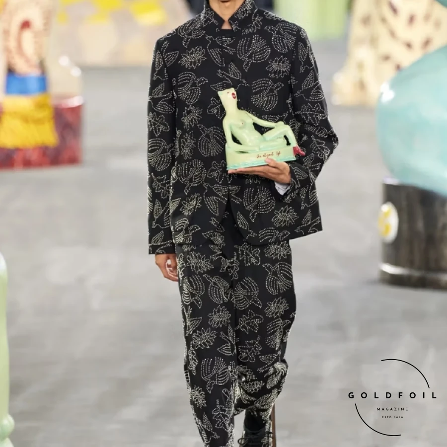 Kim Jones focused on craftsmanship and collaboration for Dior's SS25, emphasizing the skills of ateliers and artisans. Partnering with South African ceramicist Hylton Nel, Jones presented a collection celebrating work and personal expression, drawing parallels between Christian Dior, Nel, and himself. Nel's oversized cat statues adorned the runway alongside Jones' designs, which featured muted tones with vibrant accents like fluorescent vests and baby blue jackets. Nel's artwork also graced sweater vests and accessories, including a standout 70s-inspired drawstring collar, enriching the collection with artistic flair. Kim Jones focused on craftsmanship and collaboration for Dior's SS25, emphasizing the skills of ateliers and artisans. Partnering with South African ceramicist Hylton Nel, Jones presented a collection celebrating work and personal expression, drawing parallels between Christian Dior, Nel, and himself. Nel's oversized cat statues adorned the runway alongside Jones' designs, which featured muted tones with vibrant accents like fluorescent vests and baby blue jackets. Nel's artwork also graced sweater vests and accessories, including a standout 70s-inspired drawstring collar, enriching the collection with artistic flair.