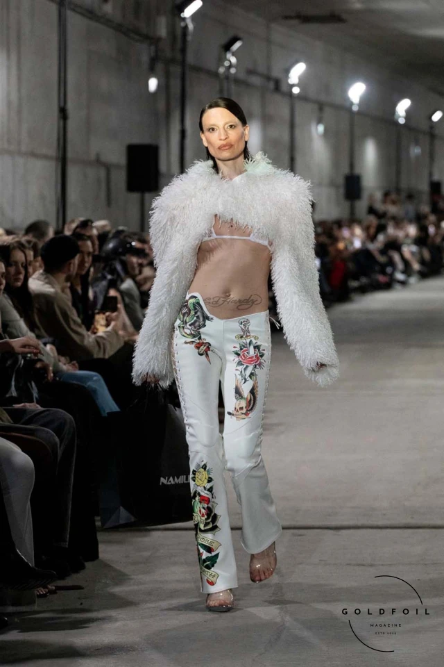 Namilia’s Spring/Summer 2025 runway show at Berlin Fashion Week was a visionary spectacle that fused futuristic design with potent social commentary. Designers Nan Li and Emilia Pfohl showcased a collection featuring high-tech fabrics, bold silhouettes, and symbolic embellishments depicting feminist icons. The use of biodegradable plastics, LED-embedded fabrics, and 3D-printed accessories highlighted the brand's commitment to sustainability, while oversized visors, holographic boots, and avant-garde jewellery added to the futuristic aesthetic. Multimedia presentations on gender equality, body positivity, and climate change underscored the show’s activist message, earning critical acclaim and reinforcing Namilia’s reputation for pushing fashion’s boundaries and inspiring change. Namilia’s Spring/Summer 2025 runway show at Berlin Fashion Week was a visionary spectacle that fused futuristic design with potent social commentary. Designers Nan Li and Emilia Pfohl showcased a collection featuring high-tech fabrics, bold silhouettes, and symbolic embellishments depicting feminist icons. The use of biodegradable plastics, LED-embedded fabrics, and 3D-printed accessories highlighted the brand's commitment to sustainability, while oversized visors, holographic boots, and avant-garde jewellery added to the futuristic aesthetic. Multimedia presentations on gender equality, body positivity, and climate change underscored the show’s activist message, earning critical acclaim and reinforcing Namilia’s reputation for pushing fashion’s boundaries and inspiring change.