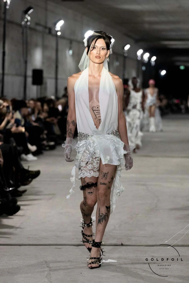 Namilia’s Spring/Summer 2025 runway show at Berlin Fashion Week was a visionary spectacle that fused futuristic design with potent social commentary. Designers Nan Li and Emilia Pfohl showcased a collection featuring high-tech fabrics, bold silhouettes, and symbolic embellishments depicting feminist icons. The use of biodegradable plastics, LED-embedded fabrics, and 3D-printed accessories highlighted the brand's commitment to sustainability, while oversized visors, holographic boots, and avant-garde jewellery added to the futuristic aesthetic. Multimedia presentations on gender equality, body positivity, and climate change underscored the show’s activist message, earning critical acclaim and reinforcing Namilia’s reputation for pushing fashion’s boundaries and inspiring change. Namilia’s Spring/Summer 2025 runway show at Berlin Fashion Week was a visionary spectacle that fused futuristic design with potent social commentary. Designers Nan Li and Emilia Pfohl showcased a collection featuring high-tech fabrics, bold silhouettes, and symbolic embellishments depicting feminist icons. The use of biodegradable plastics, LED-embedded fabrics, and 3D-printed accessories highlighted the brand's commitment to sustainability, while oversized visors, holographic boots, and avant-garde jewellery added to the futuristic aesthetic. Multimedia presentations on gender equality, body positivity, and climate change underscored the show’s activist message, earning critical acclaim and reinforcing Namilia’s reputation for pushing fashion’s boundaries and inspiring change.