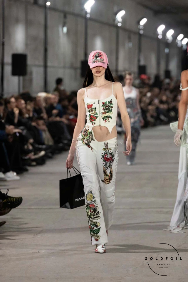 Namilia’s Spring/Summer 2025 runway show at Berlin Fashion Week was a visionary spectacle that fused futuristic design with potent social commentary. Designers Nan Li and Emilia Pfohl showcased a collection featuring high-tech fabrics, bold silhouettes, and symbolic embellishments depicting feminist icons. The use of biodegradable plastics, LED-embedded fabrics, and 3D-printed accessories highlighted the brand's commitment to sustainability, while oversized visors, holographic boots, and avant-garde jewellery added to the futuristic aesthetic. Multimedia presentations on gender equality, body positivity, and climate change underscored the show’s activist message, earning critical acclaim and reinforcing Namilia’s reputation for pushing fashion’s boundaries and inspiring change. Namilia’s Spring/Summer 2025 runway show at Berlin Fashion Week was a visionary spectacle that fused futuristic design with potent social commentary. Designers Nan Li and Emilia Pfohl showcased a collection featuring high-tech fabrics, bold silhouettes, and symbolic embellishments depicting feminist icons. The use of biodegradable plastics, LED-embedded fabrics, and 3D-printed accessories highlighted the brand's commitment to sustainability, while oversized visors, holographic boots, and avant-garde jewellery added to the futuristic aesthetic. Multimedia presentations on gender equality, body positivity, and climate change underscored the show’s activist message, earning critical acclaim and reinforcing Namilia’s reputation for pushing fashion’s boundaries and inspiring change.