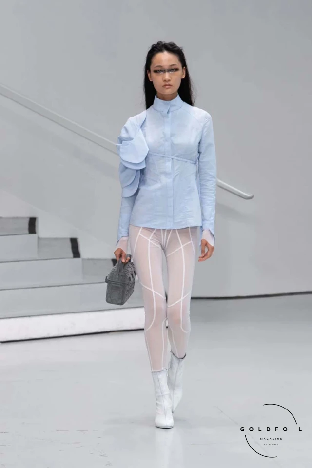 Yenesai’s latest collection, inspired by the desert biome, offers innovative solutions and challenges through color theory, soft fabrics, refined basics, and explorative accessories tailored for the future nomad. Emphasizing functionality, the collection includes garments that facilitate movement and action, while incorporating harvested resources like crystals and essential oils in their new clear resin canister bag. Advances in 3D-printed accessories, including a cyborg hand clasp and redesigned eyewear, reflect the nomad’s evolving relationship with the environment, showcased in shiny, flecked fabrics and gemstone-inspired textures. The show concludes with leather looks featuring intricate paneling and armor-style layering. Yenesai, named after the Yenesai River, blends futuristic vision with ancestral nomadic values, offering technical fabrics and striking silhouettes for a global community of travelers, and fostering creative collaboration through retreats and events. Yenesai’s latest collection, inspired by the desert biome, offers innovative solutions and challenges through color theory, soft fabrics, refined basics, and explorative accessories tailored for the future nomad. Emphasizing functionality, the collection includes garments that facilitate movement and action, while incorporating harvested resources like crystals and essential oils in their new clear resin canister bag. Advances in 3D-printed accessories, including a cyborg hand clasp and redesigned eyewear, reflect the nomad’s evolving relationship with the environment, showcased in shiny, flecked fabrics and gemstone-inspired textures. The show concludes with leather looks featuring intricate paneling and armor-style layering. Yenesai, named after the Yenesai River, blends futuristic vision with ancestral nomadic values, offering technical fabrics and striking silhouettes for a global community of travelers, and fostering creative collaboration through retreats and events.