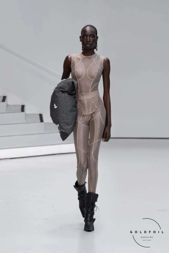 Yenesai’s latest collection, inspired by the desert biome, offers innovative solutions and challenges through color theory, soft fabrics, refined basics, and explorative accessories tailored for the future nomad. Emphasizing functionality, the collection includes garments that facilitate movement and action, while incorporating harvested resources like crystals and essential oils in their new clear resin canister bag. Advances in 3D-printed accessories, including a cyborg hand clasp and redesigned eyewear, reflect the nomad’s evolving relationship with the environment, showcased in shiny, flecked fabrics and gemstone-inspired textures. The show concludes with leather looks featuring intricate paneling and armor-style layering. Yenesai, named after the Yenesai River, blends futuristic vision with ancestral nomadic values, offering technical fabrics and striking silhouettes for a global community of travelers, and fostering creative collaboration through retreats and events. Yenesai’s latest collection, inspired by the desert biome, offers innovative solutions and challenges through color theory, soft fabrics, refined basics, and explorative accessories tailored for the future nomad. Emphasizing functionality, the collection includes garments that facilitate movement and action, while incorporating harvested resources like crystals and essential oils in their new clear resin canister bag. Advances in 3D-printed accessories, including a cyborg hand clasp and redesigned eyewear, reflect the nomad’s evolving relationship with the environment, showcased in shiny, flecked fabrics and gemstone-inspired textures. The show concludes with leather looks featuring intricate paneling and armor-style layering. Yenesai, named after the Yenesai River, blends futuristic vision with ancestral nomadic values, offering technical fabrics and striking silhouettes for a global community of travelers, and fostering creative collaboration through retreats and events.