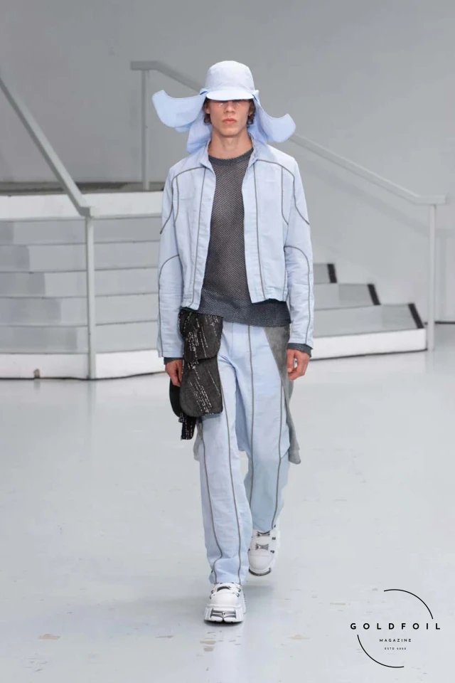 Yenesai’s latest collection, inspired by the desert biome, offers innovative solutions and challenges through color theory, soft fabrics, refined basics, and explorative accessories tailored for the future nomad. Emphasizing functionality, the collection includes garments that facilitate movement and action, while incorporating harvested resources like crystals and essential oils in their new clear resin canister bag. Advances in 3D-printed accessories, including a cyborg hand clasp and redesigned eyewear, reflect the nomad’s evolving relationship with the environment, showcased in shiny, flecked fabrics and gemstone-inspired textures. The show concludes with leather looks featuring intricate paneling and armor-style layering. Yenesai, named after the Yenesai River, blends futuristic vision with ancestral nomadic values, offering technical fabrics and striking silhouettes for a global community of travelers, and fostering creative collaboration through retreats and events. Yenesai’s latest collection, inspired by the desert biome, offers innovative solutions and challenges through color theory, soft fabrics, refined basics, and explorative accessories tailored for the future nomad. Emphasizing functionality, the collection includes garments that facilitate movement and action, while incorporating harvested resources like crystals and essential oils in their new clear resin canister bag. Advances in 3D-printed accessories, including a cyborg hand clasp and redesigned eyewear, reflect the nomad’s evolving relationship with the environment, showcased in shiny, flecked fabrics and gemstone-inspired textures. The show concludes with leather looks featuring intricate paneling and armor-style layering. Yenesai, named after the Yenesai River, blends futuristic vision with ancestral nomadic values, offering technical fabrics and striking silhouettes for a global community of travelers, and fostering creative collaboration through retreats and events.