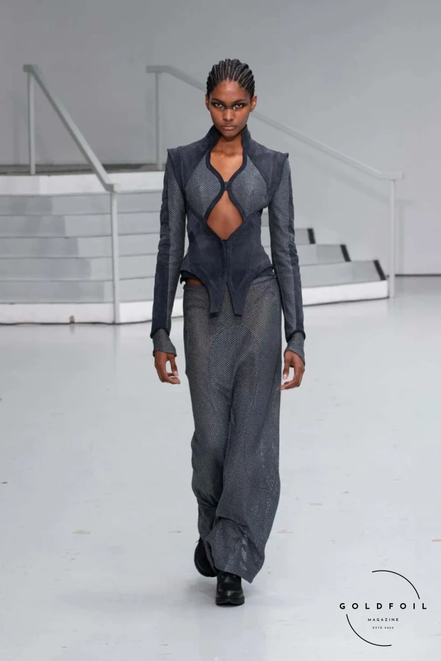 Yenesai’s latest collection, inspired by the desert biome, offers innovative solutions and challenges through color theory, soft fabrics, refined basics, and explorative accessories tailored for the future nomad. Emphasizing functionality, the collection includes garments that facilitate movement and action, while incorporating harvested resources like crystals and essential oils in their new clear resin canister bag. Advances in 3D-printed accessories, including a cyborg hand clasp and redesigned eyewear, reflect the nomad’s evolving relationship with the environment, showcased in shiny, flecked fabrics and gemstone-inspired textures. The show concludes with leather looks featuring intricate paneling and armor-style layering. Yenesai, named after the Yenesai River, blends futuristic vision with ancestral nomadic values, offering technical fabrics and striking silhouettes for a global community of travelers, and fostering creative collaboration through retreats and events. Yenesai’s latest collection, inspired by the desert biome, offers innovative solutions and challenges through color theory, soft fabrics, refined basics, and explorative accessories tailored for the future nomad. Emphasizing functionality, the collection includes garments that facilitate movement and action, while incorporating harvested resources like crystals and essential oils in their new clear resin canister bag. Advances in 3D-printed accessories, including a cyborg hand clasp and redesigned eyewear, reflect the nomad’s evolving relationship with the environment, showcased in shiny, flecked fabrics and gemstone-inspired textures. The show concludes with leather looks featuring intricate paneling and armor-style layering. Yenesai, named after the Yenesai River, blends futuristic vision with ancestral nomadic values, offering technical fabrics and striking silhouettes for a global community of travelers, and fostering creative collaboration through retreats and events.