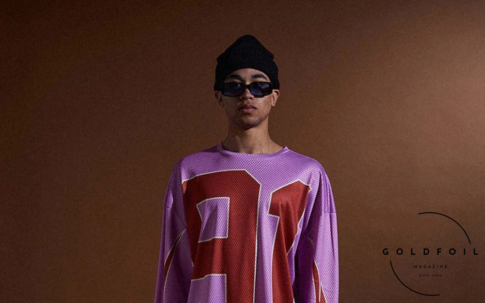 model wears a black beanie, sunglasses, a pink and red basketball top, cargo pants in leather and a tote bag. Criminal Damage, London's iconic streetwear brand established in 1991, redefines the fashion landscape with its FW24  model wears a black beanie, sunglasses, a pink and red basketball top, cargo pants in leather and a tote bag. Criminal Damage, London's iconic streetwear brand established in 1991, redefines the fashion landscape with its FW24