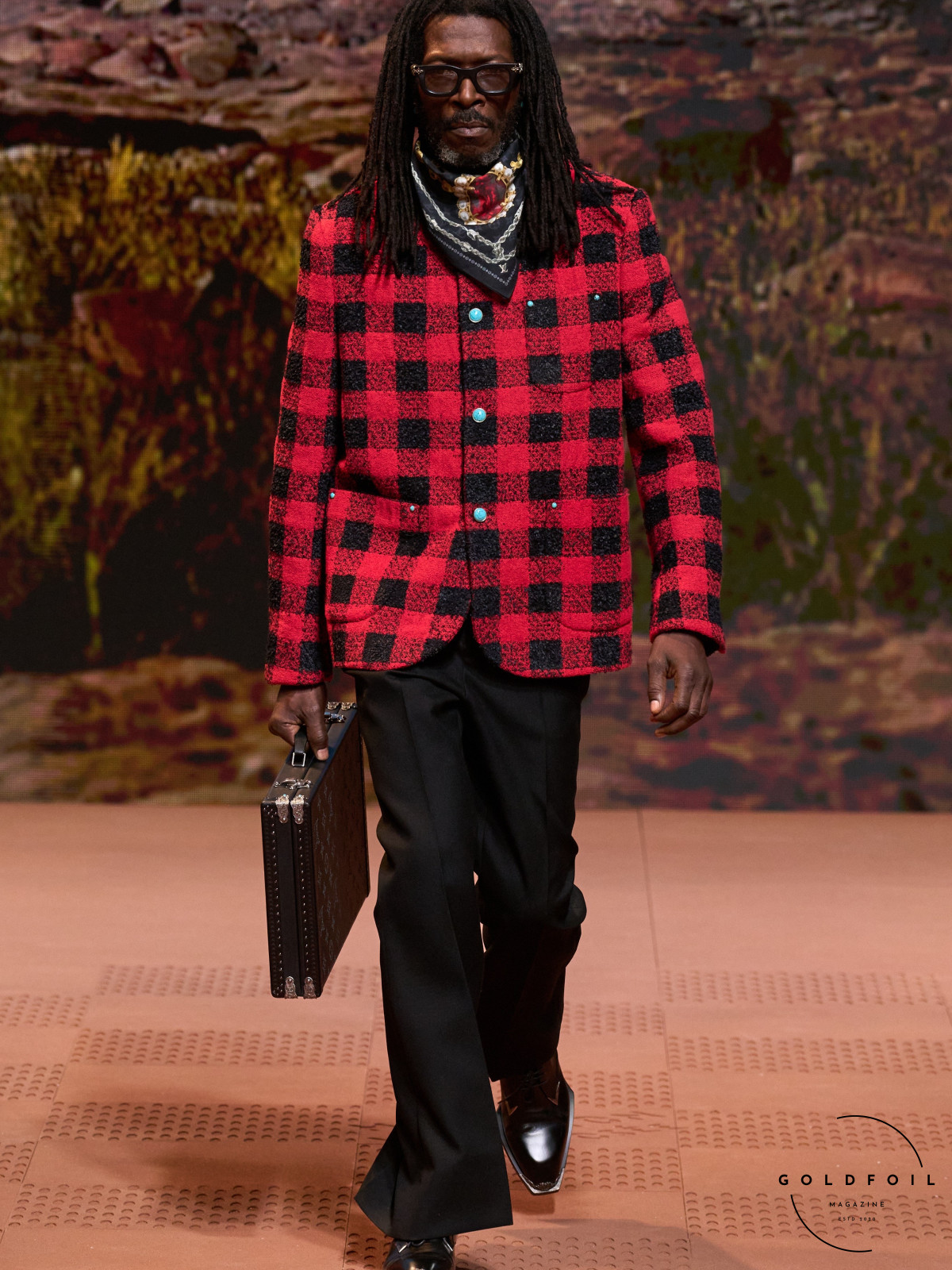 A Louis Vuitton checkered brief case, smart black trousers and a jacquard red and black boxy jacket with marine blue buttons at the Louis Vuitton Autumn Winter 2024 fashion show during Paris Fashion Week. GoldFoil Magazine is a London-based fashion magazine